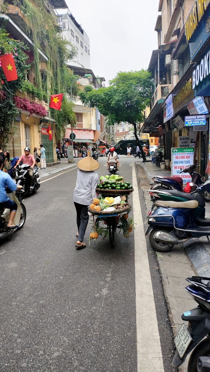 A street vendor pushes a fruit cart in Hanoi, showcasing daily life in Vietnams bustling city streets.