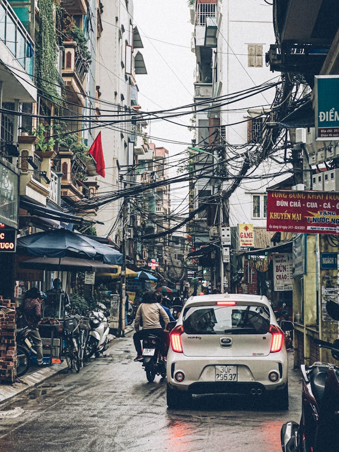 Vibrant street in Vietnam featuring cars, motorbikes, and bustling activity on a rainy day.